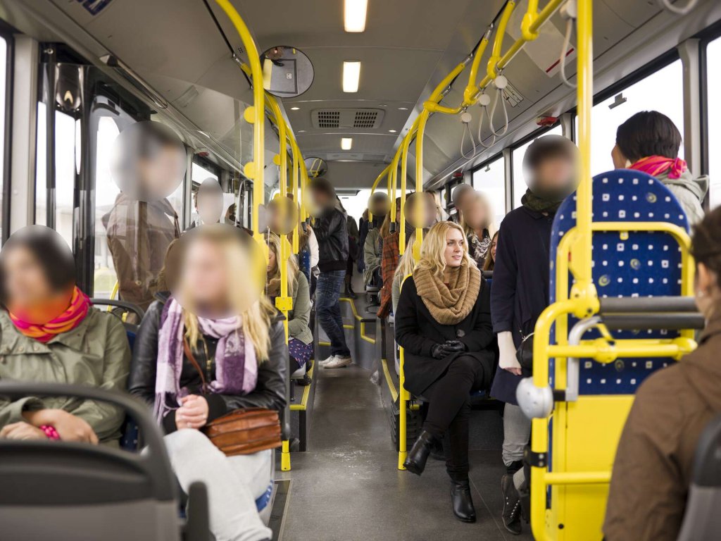 People on a bus with all faces redacted except one.